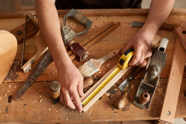 istock Closeup portrait of faceless Joiner carpenter working in his, workplace, different tools on wooden table, lot of equipments and wood, craftsman measuring wood block with tape in carpentry workshop. 1465762273