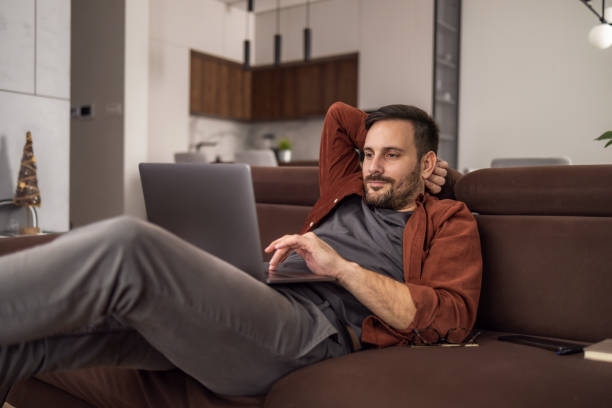 istock Young freelancer is smiling, typing on his laptop in nice modern home 1465764449