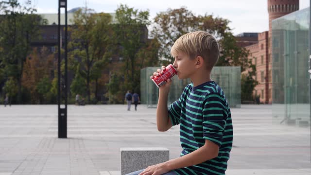 Boy child drinking a can with carbonated cola drink in city public place