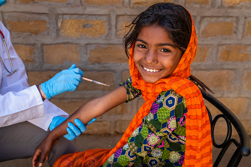 Female caucasian doctor vaccinating young Indian girl in small village, Rajasthan, India