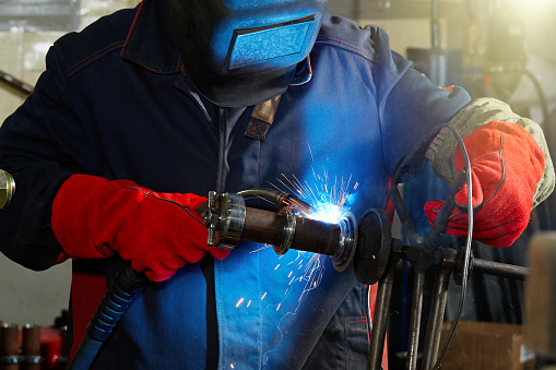 Closeup front view of unrecognizable worker welding two metal plates with gas welding machine.He's wearing welding mask and protective workwear and gloves.  Long exposure
