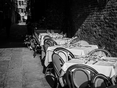 Black and white photo of restaurant tables set outdoors in the street.