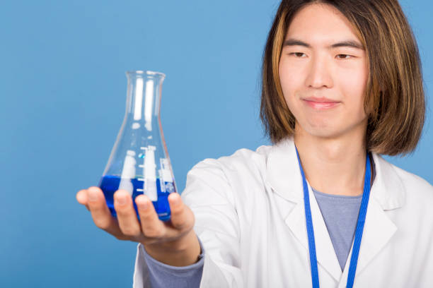 Studio portrait with blue background of an asian scientist holding a glass flask containing blue liquid