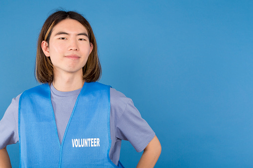 Studio portrait with blue background of a Close up portrait of an asian volunteer wearing a waistcoat