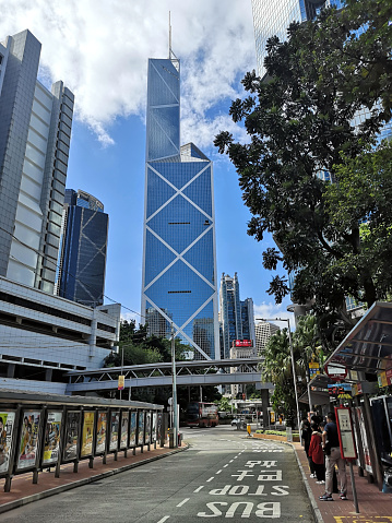 Road under the iconic bank of China tower, Hong Kong island. People standing at bus stop.