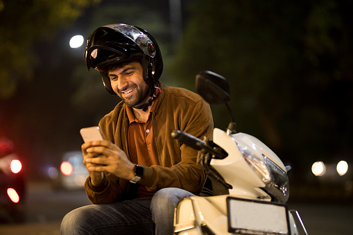 Happy man messaging on mobile phone while sitting on motor scooter outdoors at night