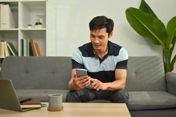 istock Handsome man chatting online, typing text message on mobile phone while sitting in living room. 1465786690
