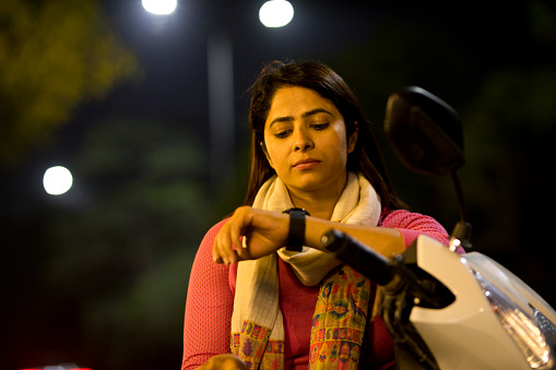 Young woman checking the time on scooter at night