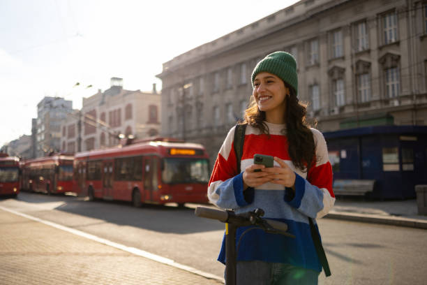 Happy female commuter with push scooter using cell phone in the city.