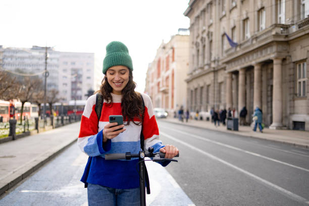 istock Happy woman using smart phone while walking with push scooter on the street. 1465787592