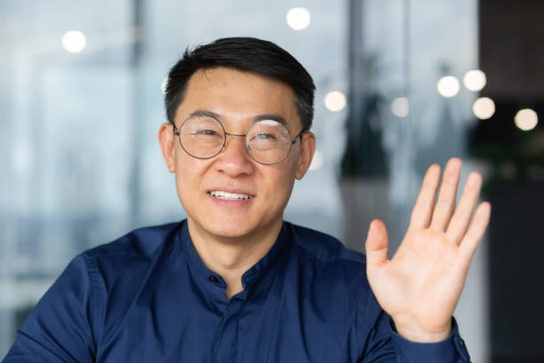 istock A successful Asian man inside the office is looking at the web camera, talking on a video call with colleagues, gesturing and smiling an online meeting with partners, talking to customers, pov. 1465787864
