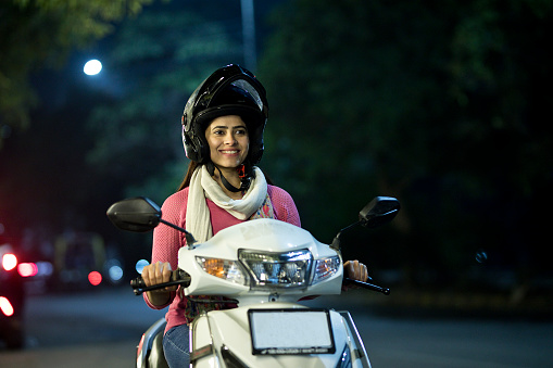 Smiling woman enjoying riding a scooter with helmet at night
