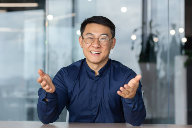 istock A successful Asian man inside the office is looking at the web camera, talking on a video call with colleagues, gesturing and smiling an online meeting with partners, talking to customers, pov. 1465787891