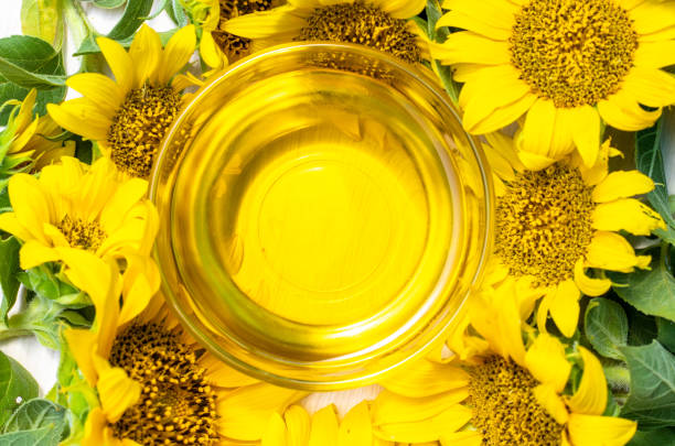 ガラスのボウルにひまわり油とたくさんの小さな小さなひまわりの黄色い植物がテキストの空き領域をモックアップ - ヒマワリ種子油 ストックフォトと画像