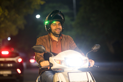 Smiling man enjoying riding a scooter with helmet at night