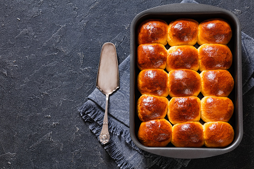 Hawaiian sweet rolls, portuguese sweet bread, soft and stretchy buns in baking dish on concrete table with cake shovel, horizontal view from above, flat lay, free space