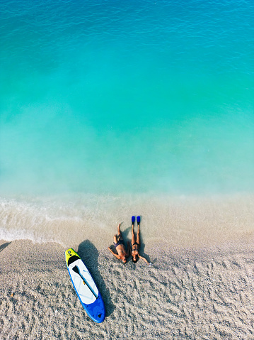 Mature couple enjoying vacation and lying and relaxing alone on the beautiful beach. Standup paddleboard is next to them and color of water is amazing. Porto Katsiki beach, Lefkada Island, Greece