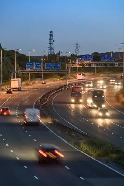 Vehicles move quickly past an intersection on the M5 motorway near Bristol, UK during the early evening. Blurred lights and light trails show speed.