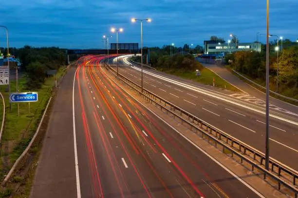 Fast moving traffic drives along the M5 motorway and highway road in UK. Light trails and streaks illustrate the illusion of speed using long exposure