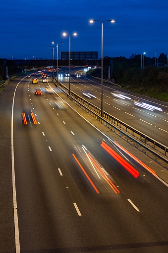 Fast moving traffic drives along the M5 motorway and highway road in UK. Light trails and streaks illustrate the illusion of speed using long exposure