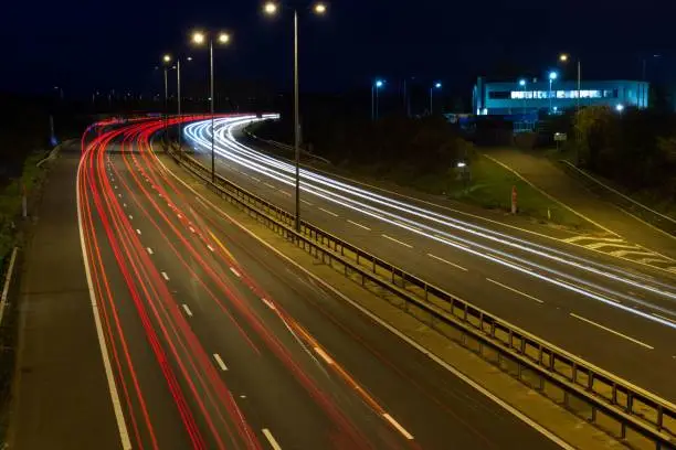 Fast moving traffic drives along the M5 motorway and highway road in UK. Light trails and streaks illustrate the illusion of speed using long exposure