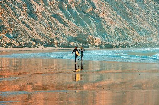 Imsouane, Morocco – December 20, 2022: Two surfers walking towards the waves of the beach, carrying their surfboards in their hands