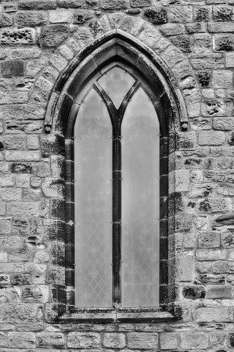 A vertical shot of medieval gothic-style arch church window, grayscale shot