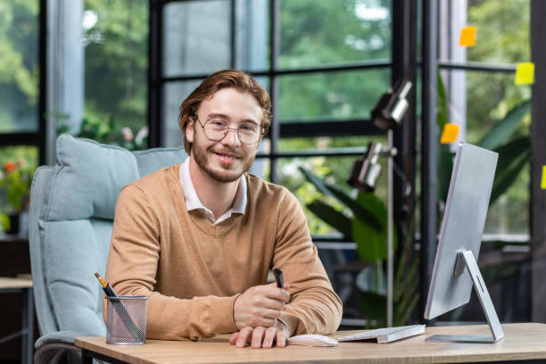 istock Portrait of successful smiling programmer inside modern green loft office, blond man smiling and looking at camera, businessman in sweater and casual shirt close up working with computer 1465802452