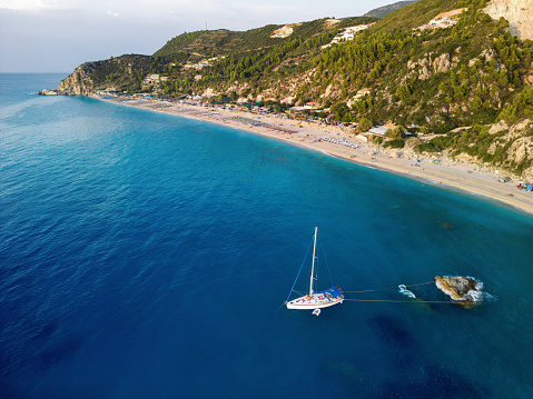 Sailboat anchored and fasten for rocks near coast in peaceful bay on Lefkada island, Greece. Drone point of view