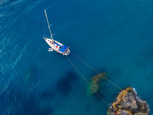 Sailboat anchored and fasten for rocks near coast in peaceful bay on Lefkada island, Greece. Drone point of view