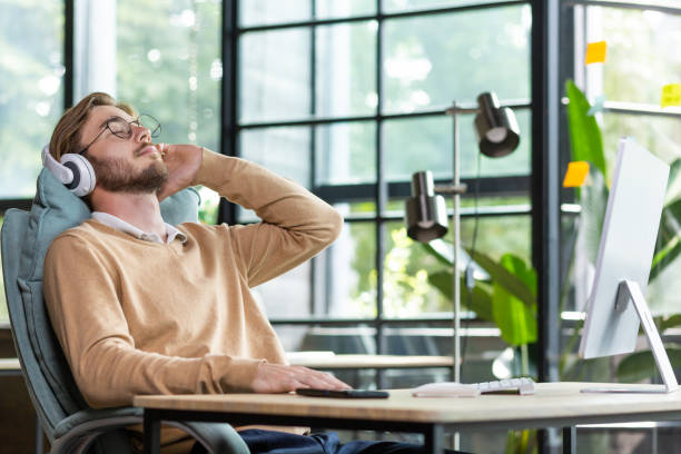 istock Young businessman man resting from work, overtime, break. Sitting in the office at a table with a computer, leaning back in a chair, listening to music in headphones, closed his eyes, relaxed 1465803471