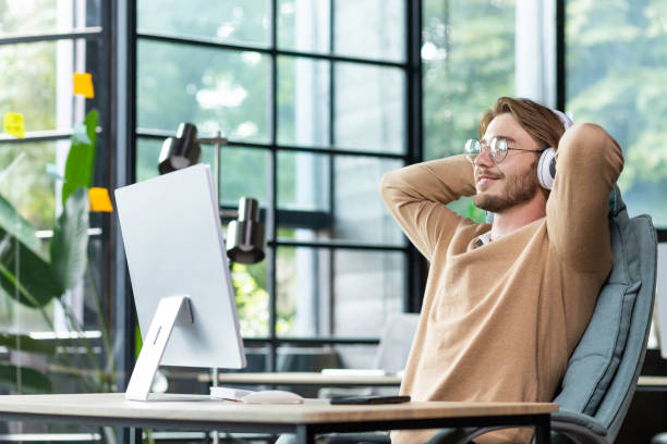 istock Young successful man in office resting with eyes closed and hands behind head, programmer finished work satisfied with achievement results and listening to music in headphones and podcast online 1465803641