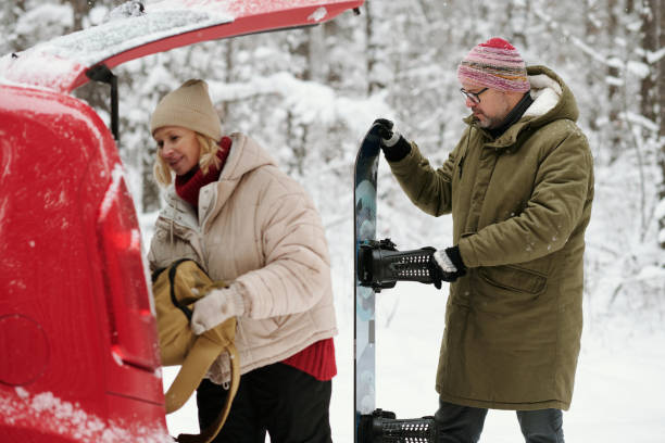 istock Man with snowboard standing behind his wife putting backpack into car trunk 1465806167
