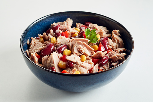 A closeup shot of a salad with corn, red beans, tiny meat slices, and lettuce in a black bowl on a white background