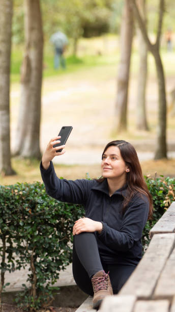 istock Vertical shot of a Hispanic brunette female using her phone while sitting in a park 1465810684