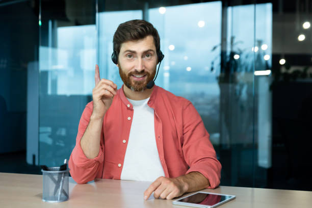 istock Webcam pov view, man in office with headset for video call smiling and looking into camera, businessman seller online communicates with customers, works remotely laptop at online meeting colleagues. 1465812327