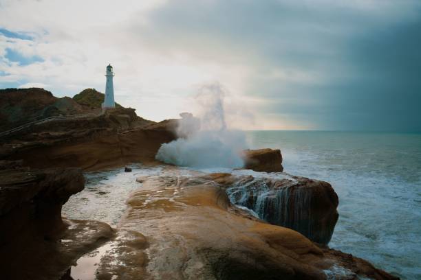 vista panoramica delle onde tempestose che si infrangono contro le formazioni rocciose e il faro di castlepoint - castlepoint foto e immagini stock