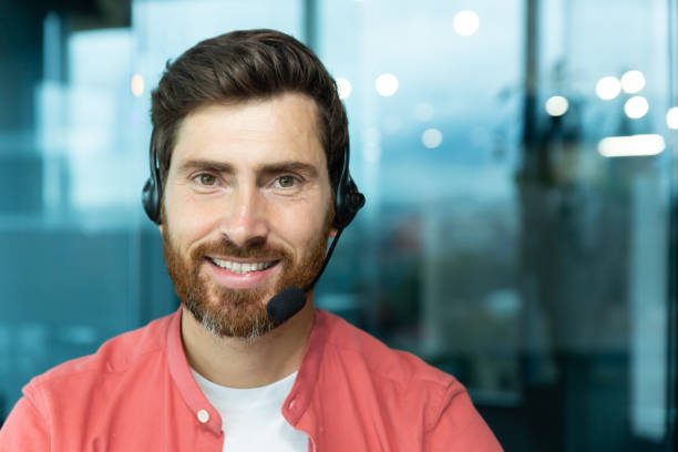 istock Close-up portrait of mature man with beard and video call headset inside office, tech support worker smiling and looking at camera in red shirt, online customer service and support 1465813672