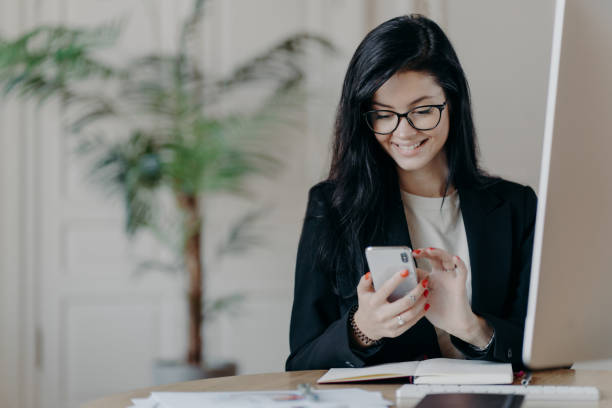 istock Beautiful smiling female freelancer works remotely, concentrated in smartphone, sends feedback on received message, sits in coworking space, dressed formally, works on computer, surfs internet 1465816276