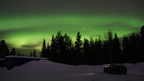 Kittila, Finland - Feb 12, 2023: Wonderful landscapes in Lapland, Finland. A solid black Tesla Model 3 under beautiful Northern Lights, Aurora Borealis. Starry sky. Clear winter night. Selective focus