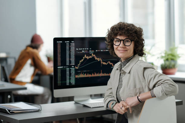 Young smiling businesswoman sitting by workplace with computer monitor stock photo