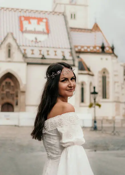 Young bride standing on street in front of church, looking at camera and smiling.