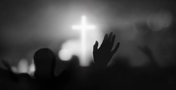 Passionate Christians raising their hands in praise, prayer and worship Passionate Christian praising with hands raised towards the cross and Holy Spirit filled gracious church worship with bokeh and silhouette background church black and white people praying stock pictures, royalty-free photos & images