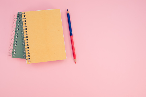 A vertical shot of closed notebook on a pink background with copy space
