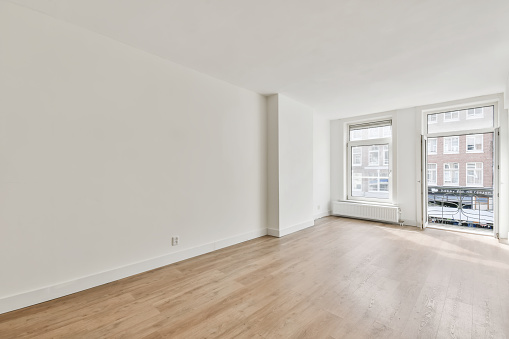 An interior shot of an empty room with white walls and a wooden floor with a balcony