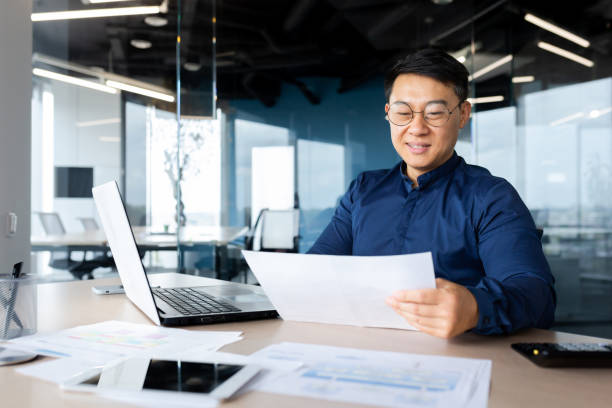 istock A young man, an Asian architect works in the office. Holds documents, plans, drawings in his hands 1465830437