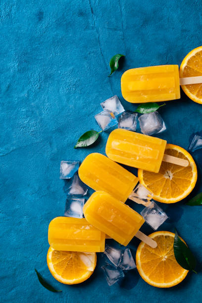 istock Ice cream popsicle orange with ice cube and green leaf on blue background 1465837099