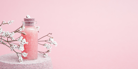 Composition with cosmetic bottle on the podium and dried flowers. Pink monochrome. Copy space, web banner