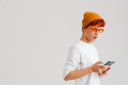 Young ginger shocked man wearing sunglasses using mobile phone isolated over white background