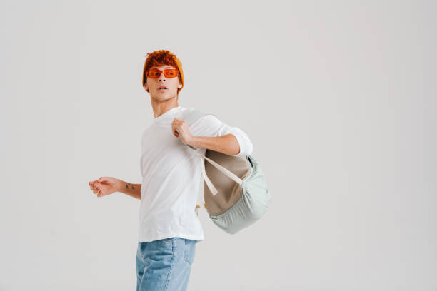 Young ginger man wearing sunglasses posing with backpack isolated over white background